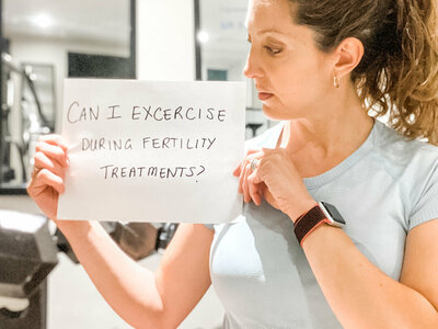 woman holding a sign that reads &quot;can i exercise during fertility treatments&quot;