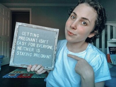infertility warrior arden cartrette holding a sign that reads "getting pregnant is easy for everyone, neither is staying pregnant"
